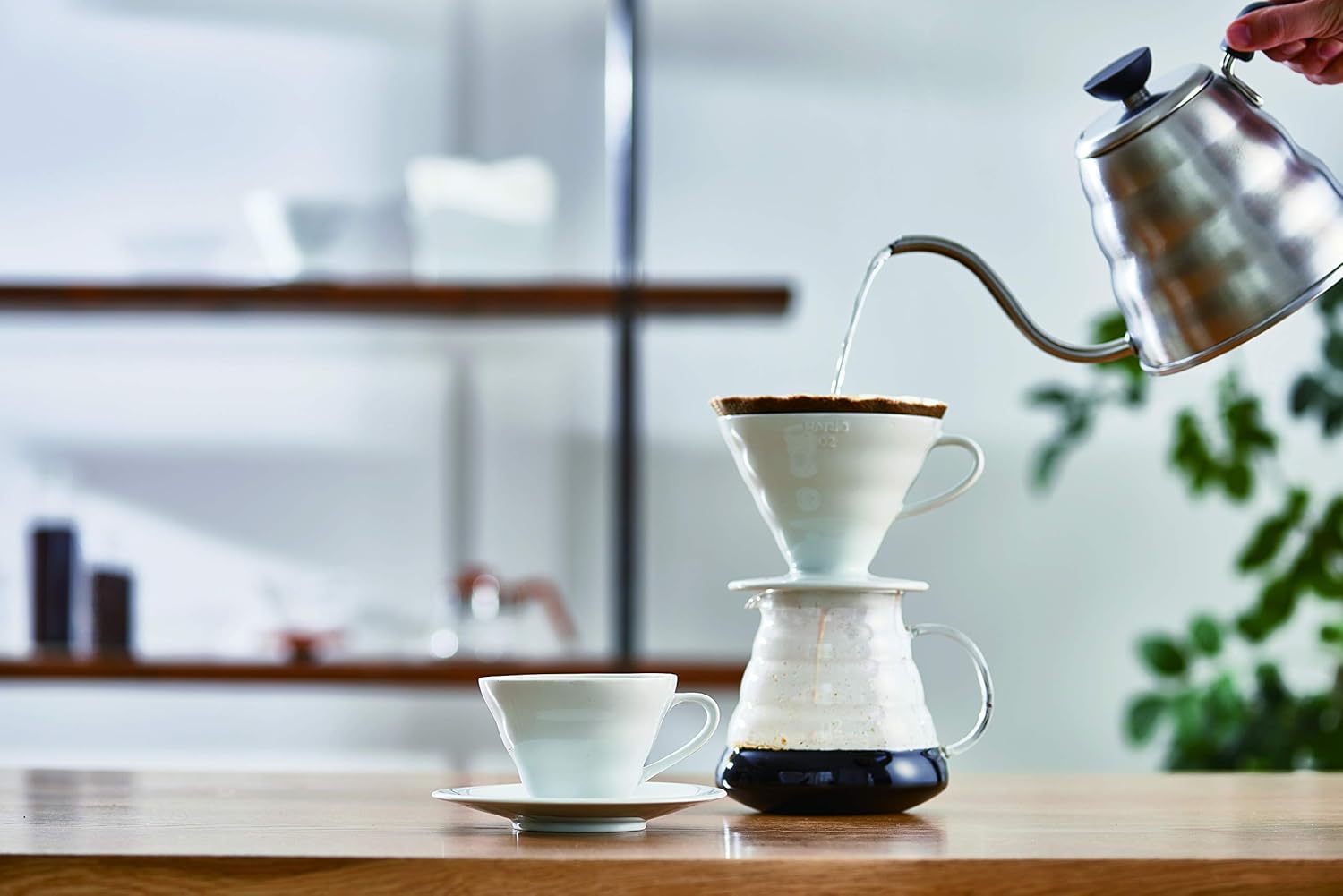 Pouring hot water from a gooseneck kettle into a Hario V60 set over a glass server