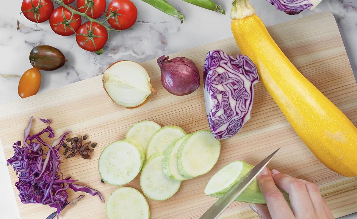 Courgette being sliced on the YAMASAN hinoki board surrounded by vegetables