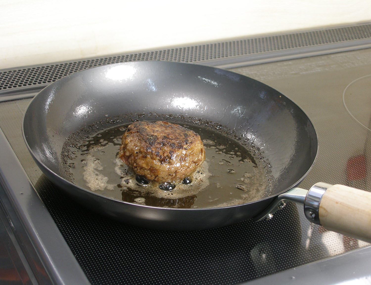 A hamburger patty searing in a River Light Kiwame iron pan on an induction cooktop