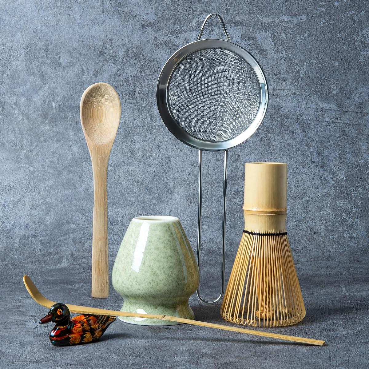 YIBO matcha kit laid out: bamboo whisk, mottled green ceramic whisk holder, steel sifter, bamboo scoop, wooden spoon and a small scoop rest