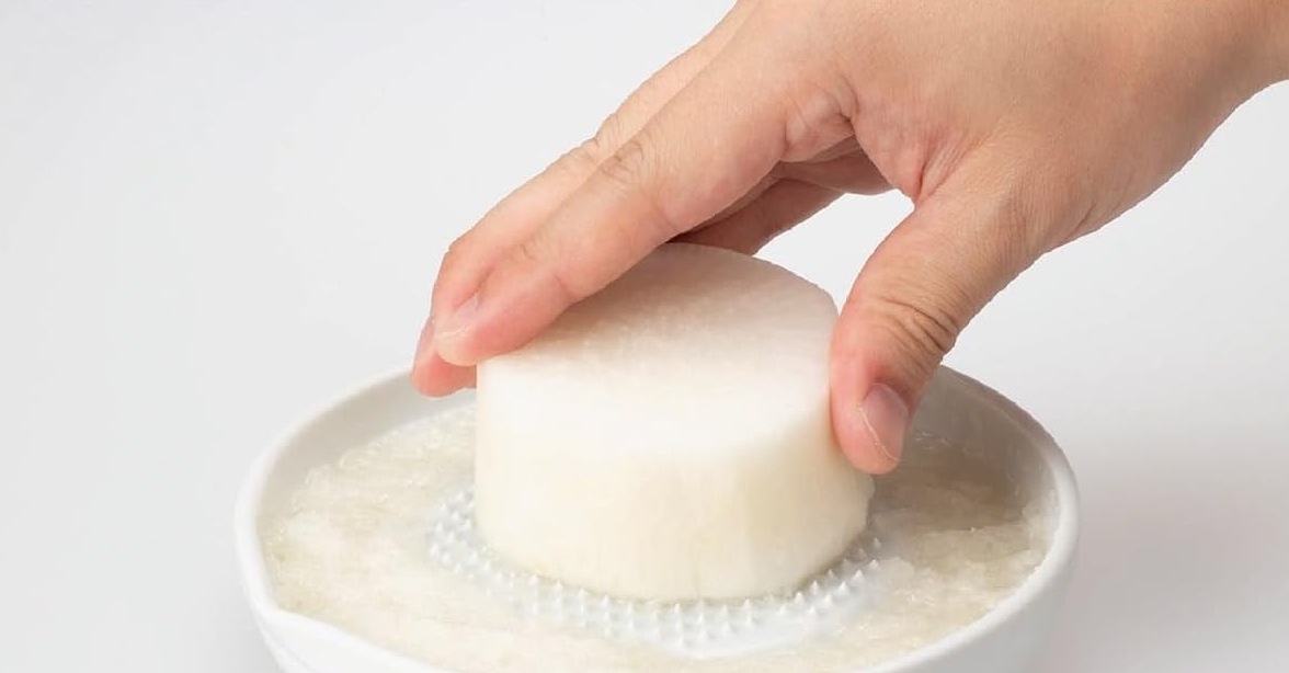 A hand rubbing a piece of daikon radish across the Kyocera ceramic grater as pulp collects in the surrounding well