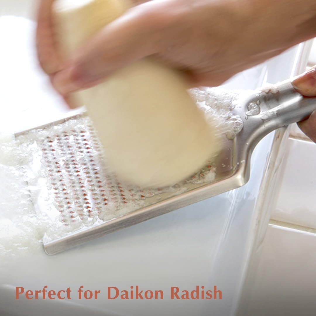 Daikon radish being grated across the stainless oroshigane with pulp gathering at the lower edge