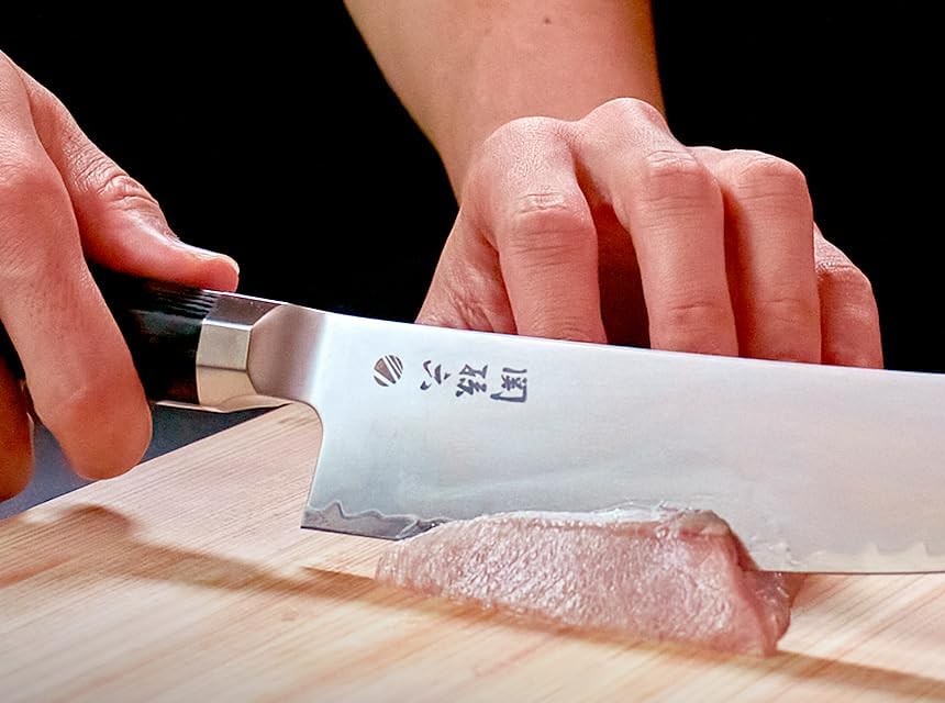 Hands pull-cutting a piece of raw fish on a wooden board with the Kaname kiritsuke