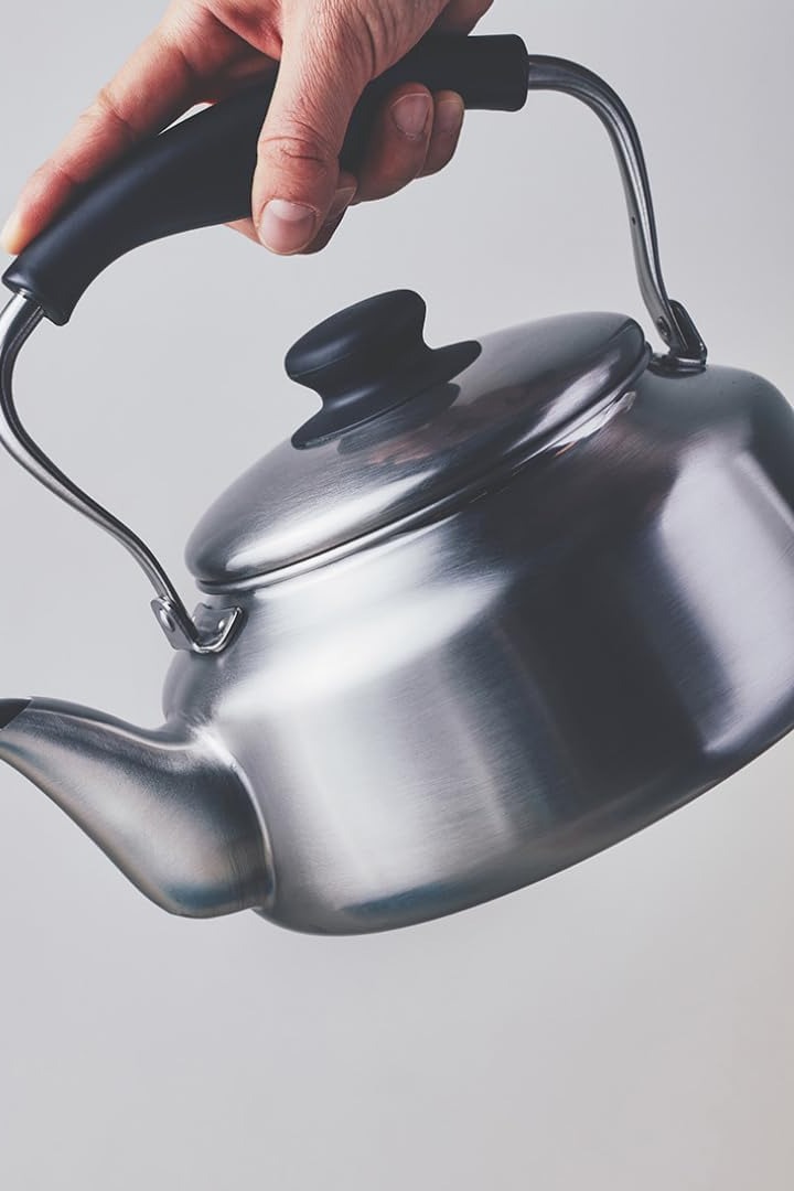 A hand lifting the Sori Yanagi kettle by its handle, ready to pour