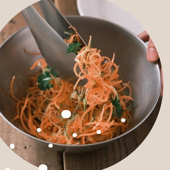 Stainless tongs tossing a shredded carrot salad in a stainless bowl