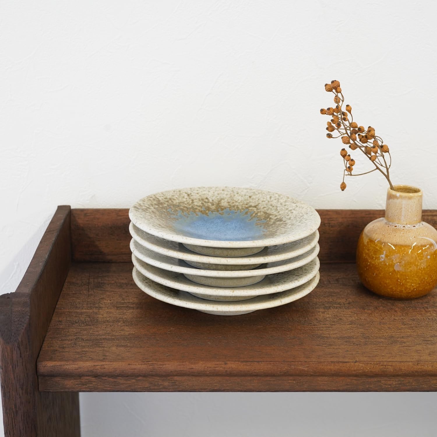 Stack of five COTONOHA plates on a wooden side table
