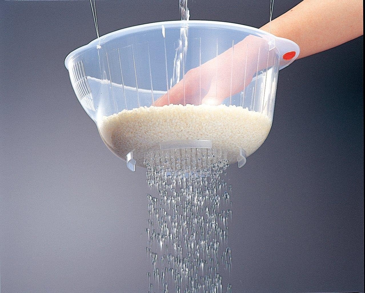 Water draining through the base of the Inomata rice washing bowl while a hand stirs white rice