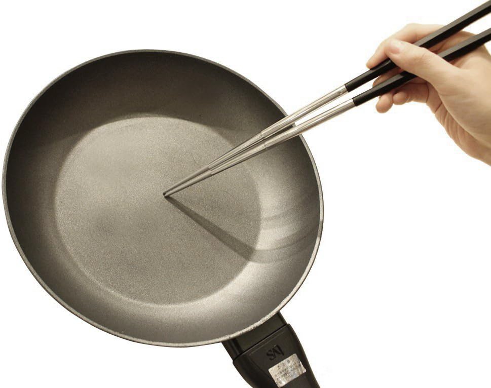 The Kai stainless saibashi reaching into a frying pan on the stove