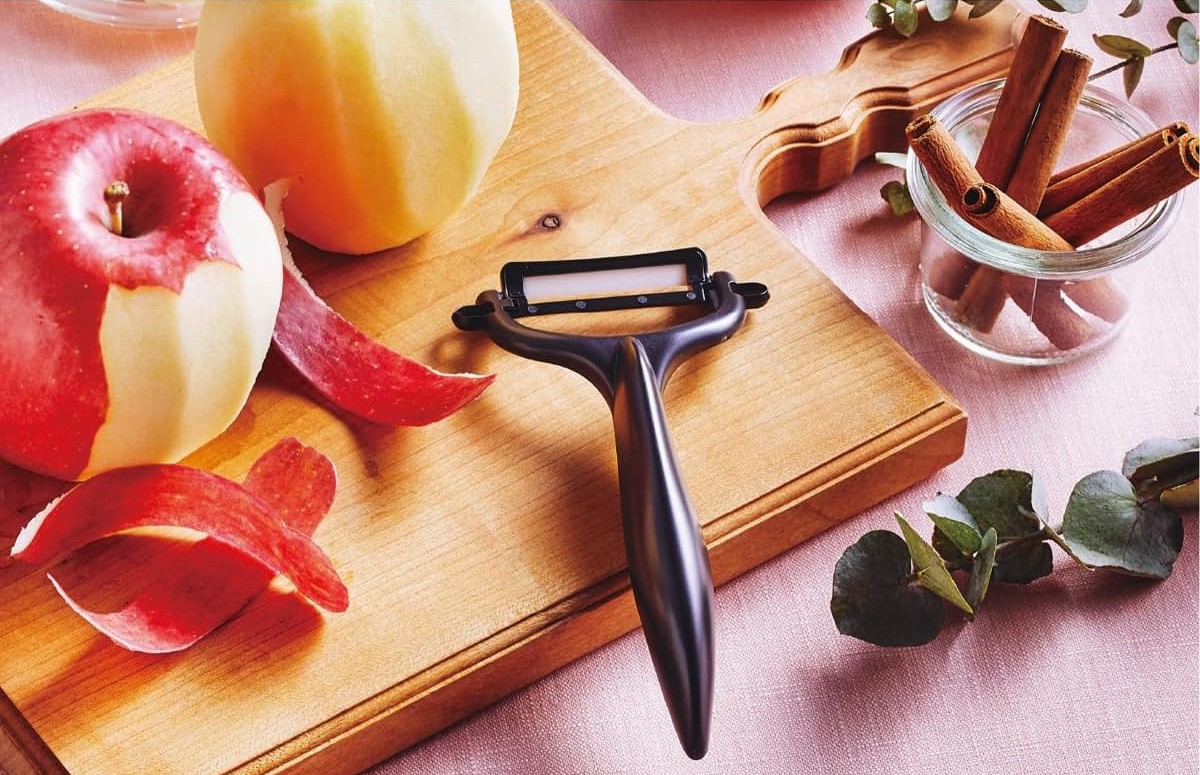 Kyocera black ceramic peeler on a wooden board beside freshly peeled apples