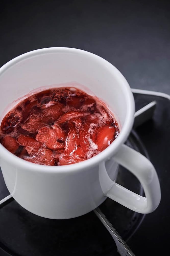 Red berries simmering in a white enamel handled stocker set on a gas burner