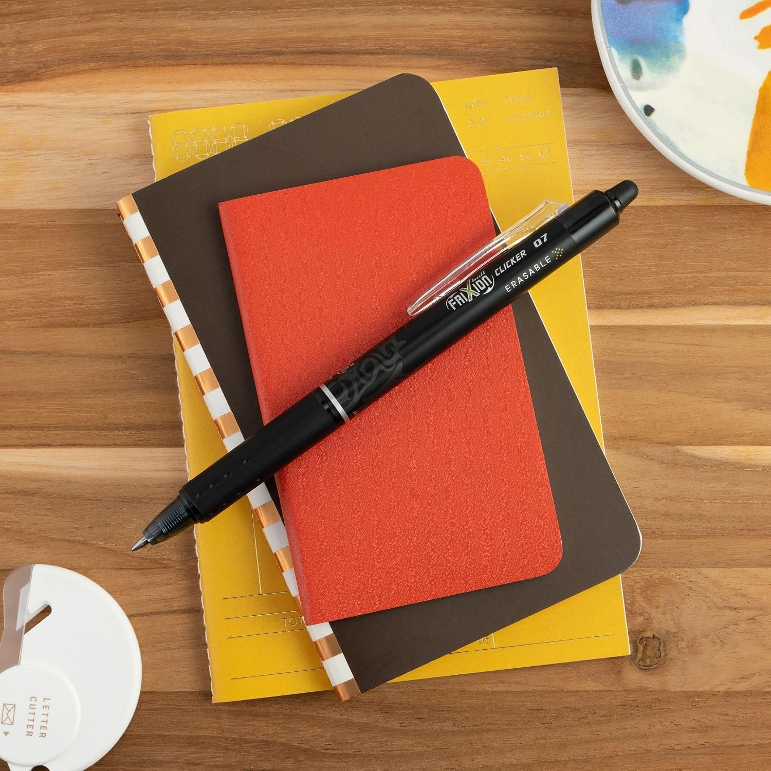 FriXion Clicker pen resting on a stack of notebooks on a wooden desk