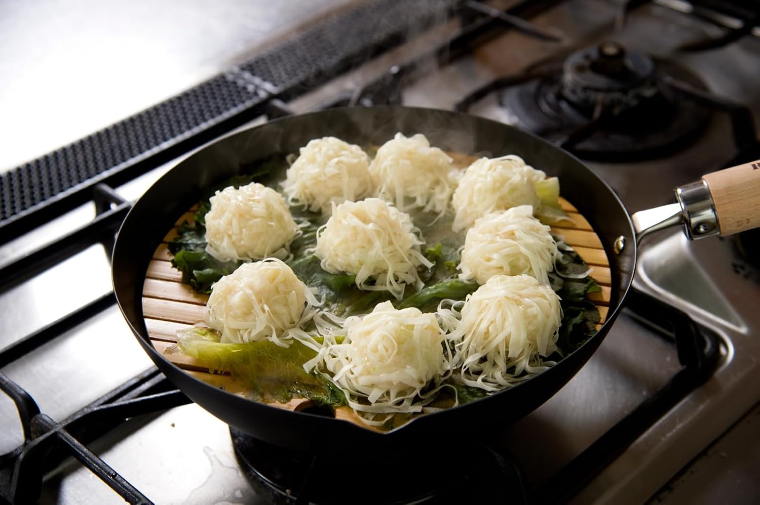 River Light bamboo steaming rack inside a black iron pan with shumai dumplings steaming on a gas stove