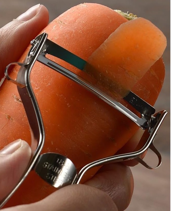 Shimomura Pro Grade peeler with a curved blade peeling a wide strip from a large carrot