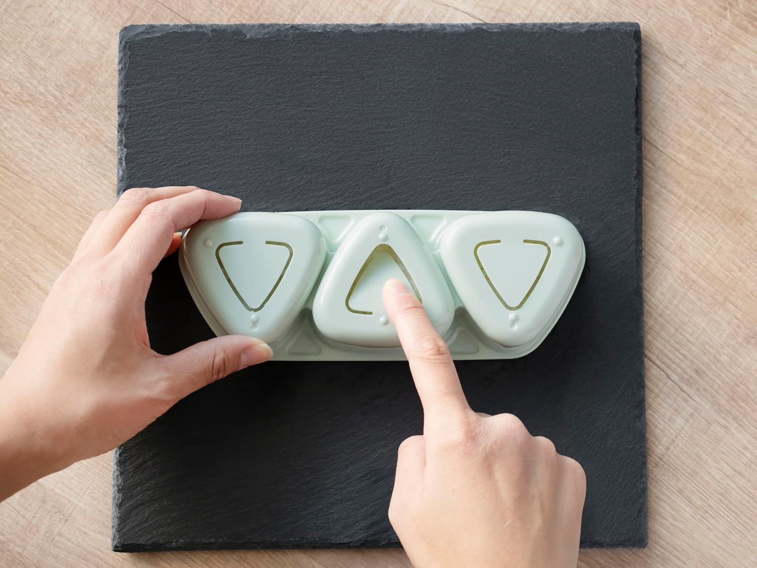 A hand pressing the lid of the Skater onigiri mold to shape three rice balls