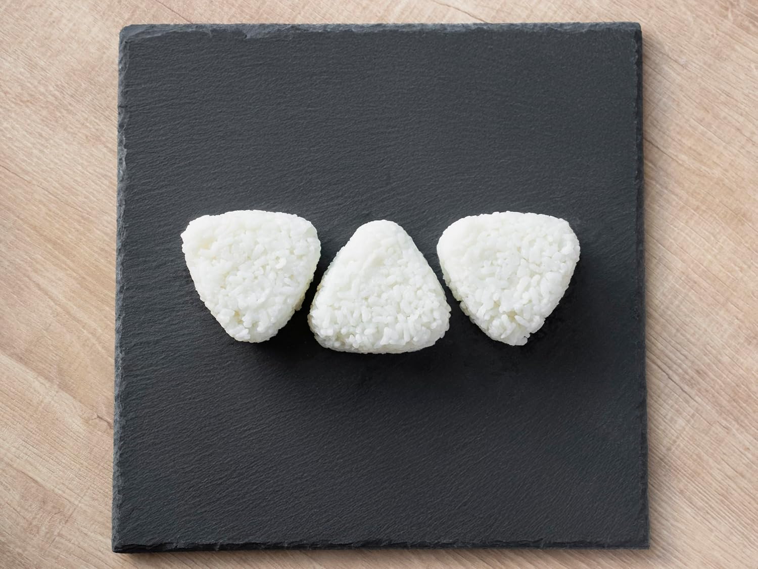 Three finished triangular onigiri from the Skater mold on a slate board