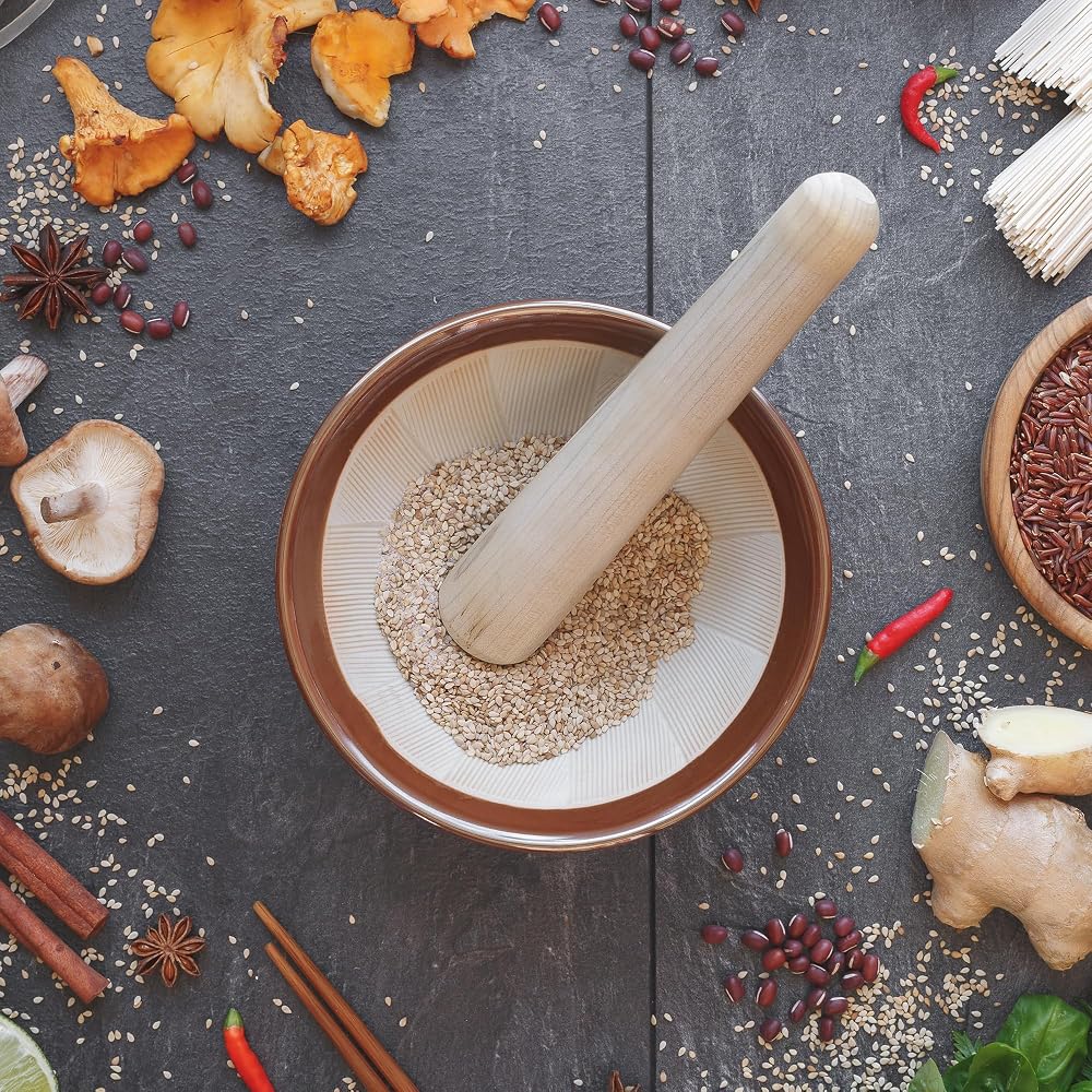 Sesame seeds being ground with a wooden pestle in a small brown suribachi surrounded by mushrooms, ginger and chilies