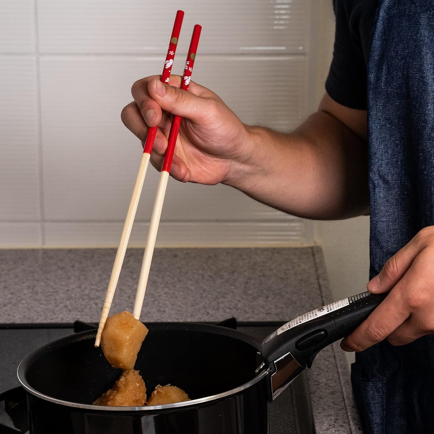 The red Tanaka Hashi saibashi lifting fried food out of a dark pot on a stove