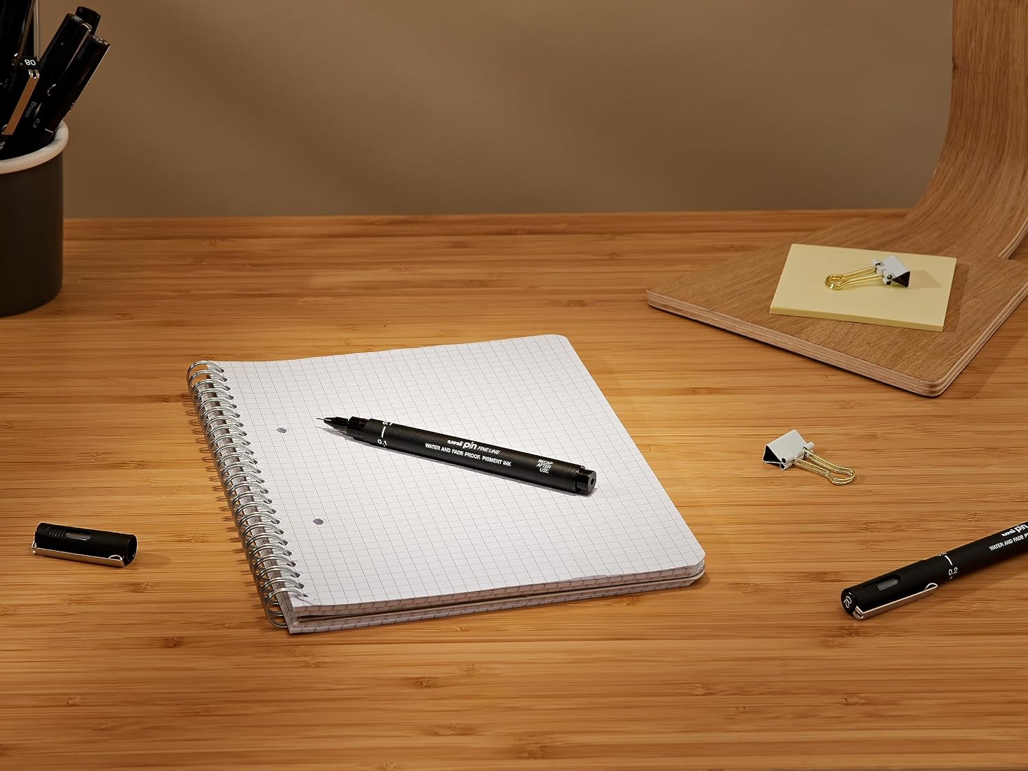 Uni Pin fineliner resting on a spiral notebook on a wooden desk